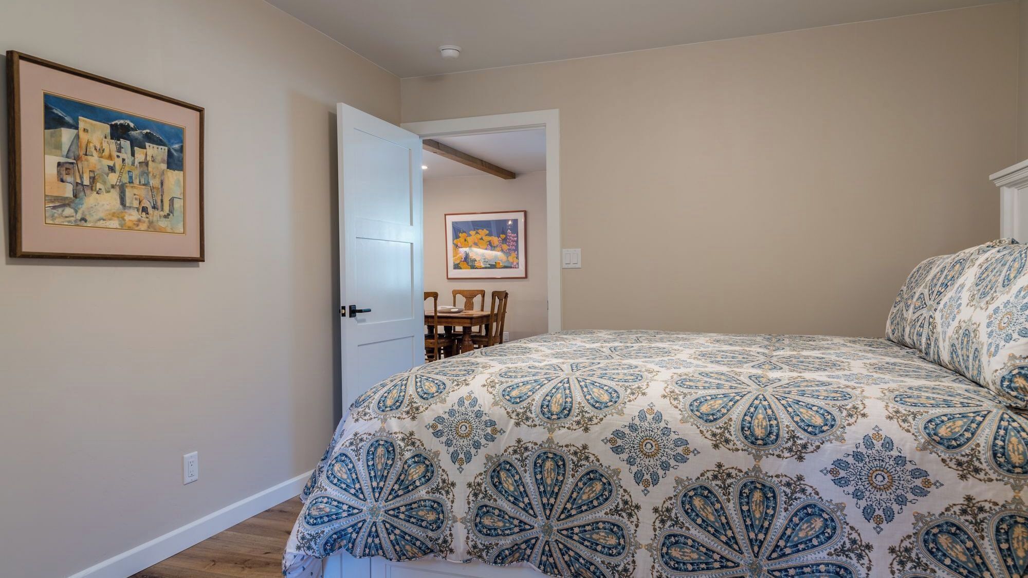 Una camera da letto con un letto grande, una porta che dà su un'area pranzo e un quadro appeso al muro.