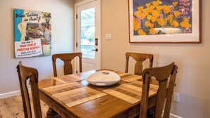 A dining area with a wooden table, four chairs, a white bowl, and two wall decorations. - The Top Shelf by Avantstay Two Master Suites + Balconies Downtown Paso Robles Wine Country (Paso Robles)