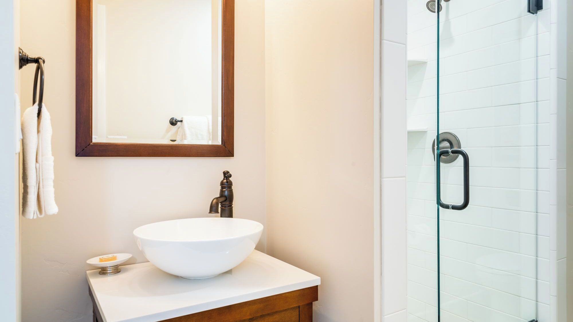 Une salle de bain avec un lavabo blanc, un meuble-lavabo en bois, un miroir et une cabine de douche en verre.