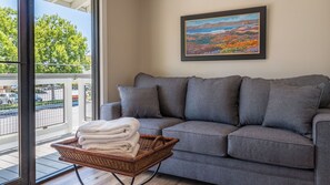 A grey sofa with multiple cushions, a wicker basket with folded towels, and a framed landscape painting on the wall. - The Top Shelf by Avantstay Two Master Suites + Balconies Downtown Paso Robles Wine Country (Paso Robles)