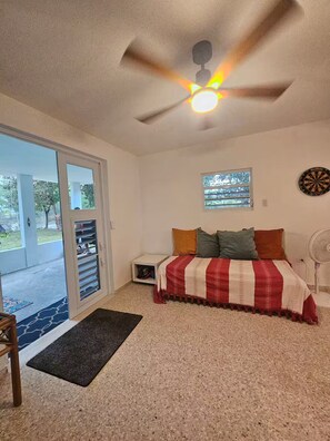 Ein Schlafzimmer mit Bett, Deckenventilator, Fenster und Dartscheibe.