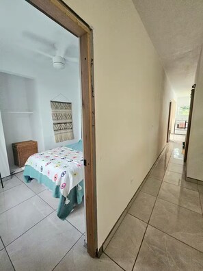 Ein Flur mit einem Bett in einem Zimmer, einem Deckenventilator und einem Wandbehang mit Muster.