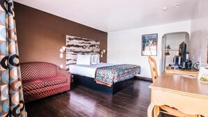 A hotel room with a bed, a sofa, a dining table, and a TV. - Accessible King Room (Anaheim)