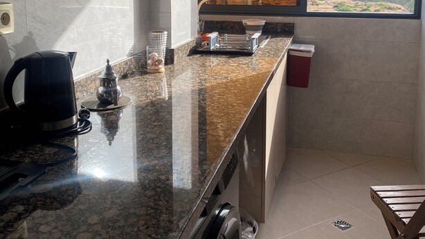 A kitchen with a granite countertop, a kettle, a small table, and a window with a view.