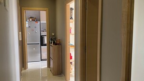 A hallway with a tiled floor leading to a kitchen area with a refrigerator and wooden cabinets.