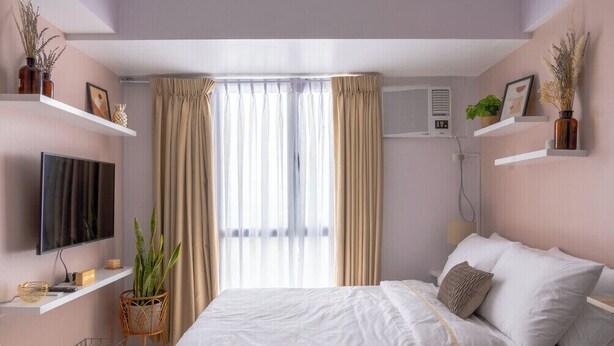 Een slaapkamer met een bed, een televisie, een raam met gordijnen en een aan de muur bevestigde airconditioning.