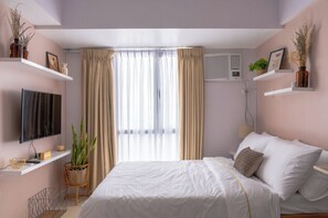 Une chambre à coucher comprenant un lit, un téléviseur, une fenêtre avec des rideaux et un climatiseur fixé au mur.