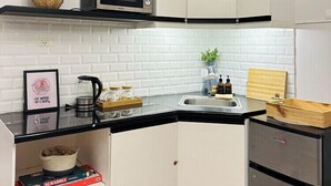 Een kleine keuken met witte kastjes, een magnetron, een spoelbak en een koelkast.