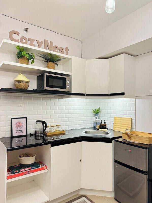 A compact kitchen with white cabinetry, a microwave, a sink, and a refrigerator.