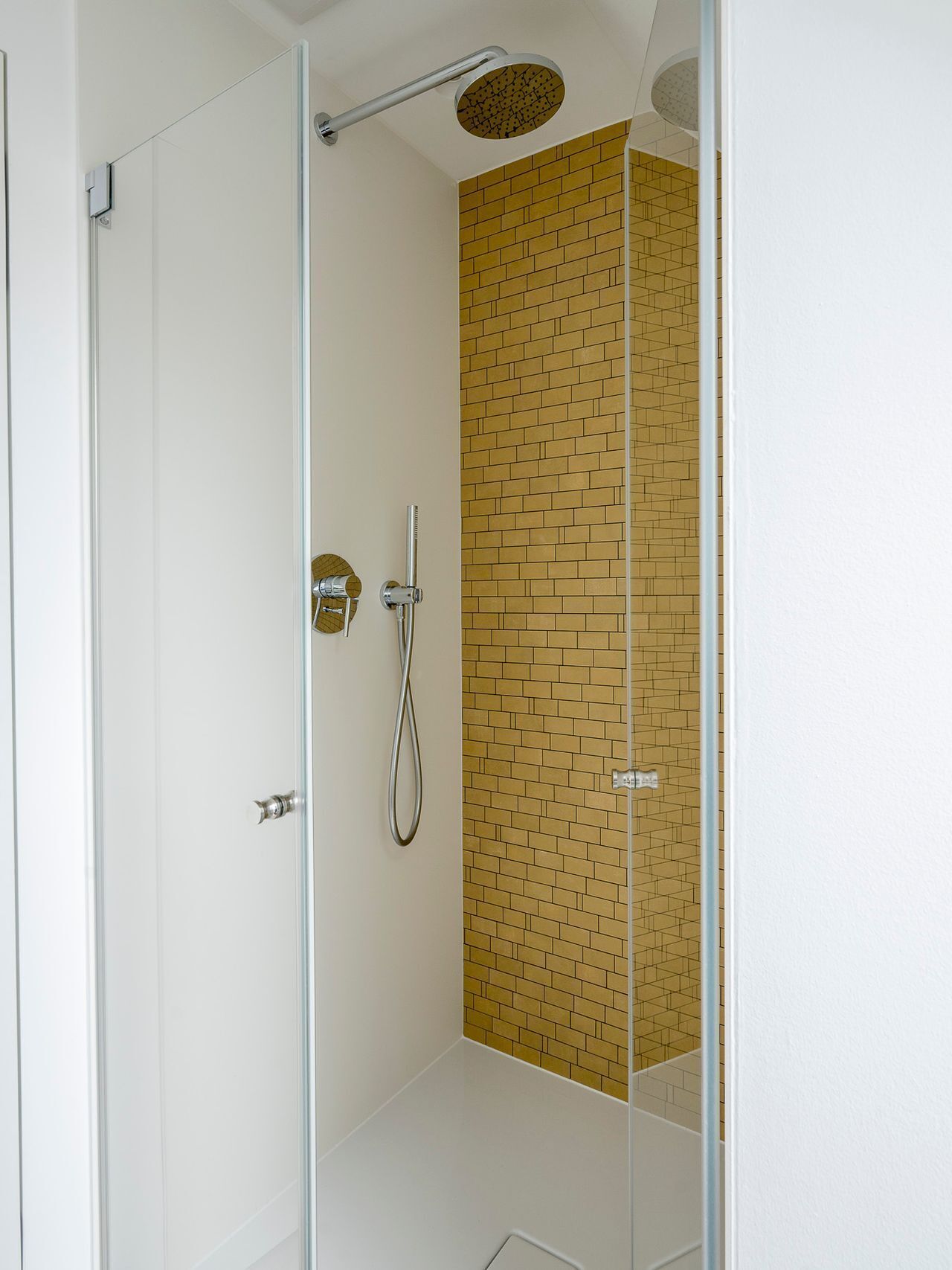 A modern shower with a glass door, a handheld showerhead, and a wall-mounted rain showerhead.
