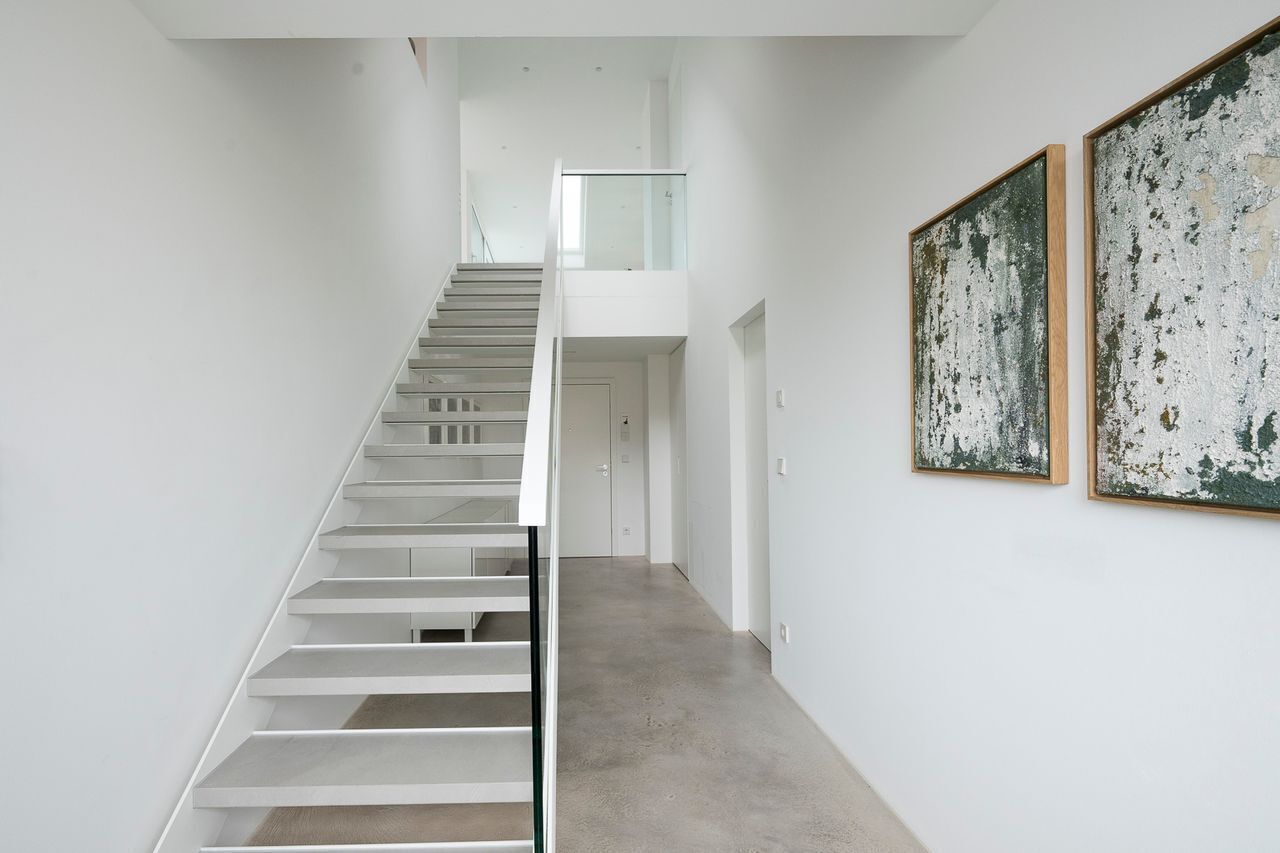 A modern interior with a staircase leading to a second floor, a glass railing, and two large abstract paintings on the wall.