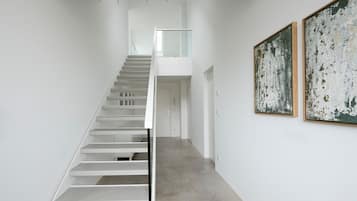 A modern interior with a staircase leading to a second floor, a glass railing, and two large abstract paintings on the wall.