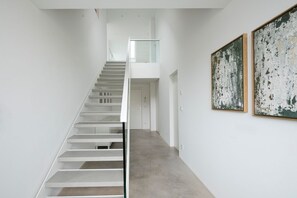 A modern interior with a staircase leading to a second floor, a glass railing, and two large abstract paintings on the wall.