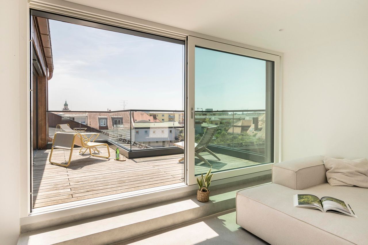 A modern living room with a large sliding glass door leading to a balcony, a sofa, a small table, and a potted plant.