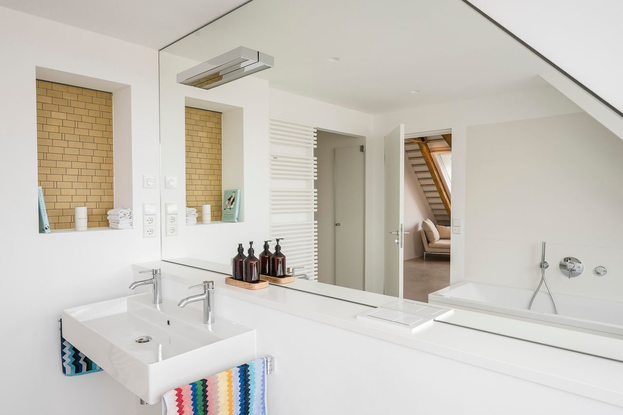 A modern bathroom with a large mirror, two sinks, and a bathtub.