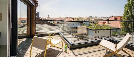 A modern balcony with glass railings, wooden flooring, and two lounge chairs.