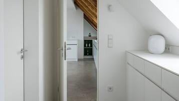 A narrow hallway with a sloped ceiling leading to a kitchen area.