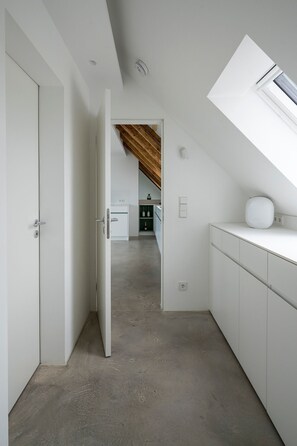 A narrow hallway with a sloped ceiling leading to a kitchen area.