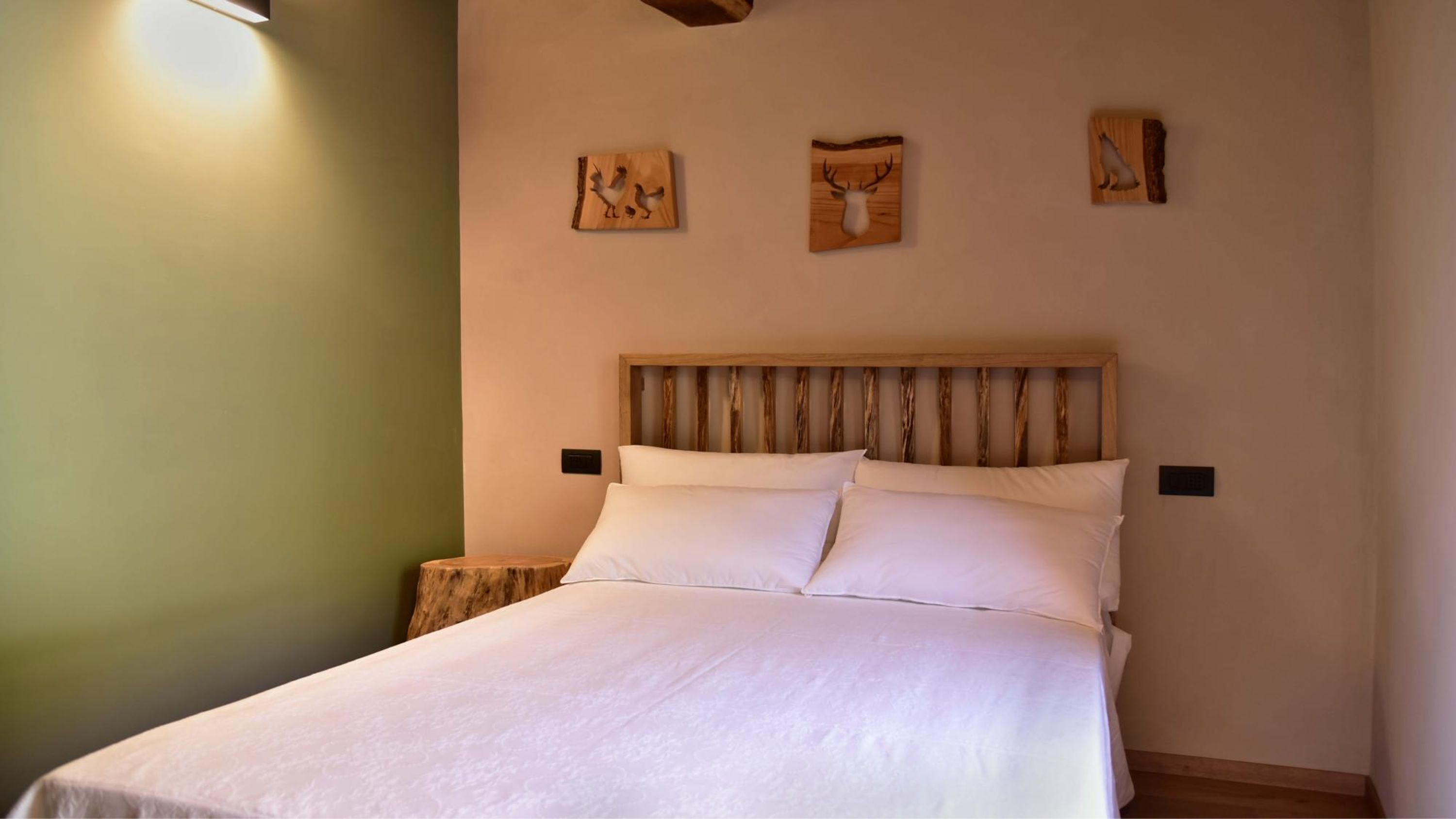 Una cama bien tendida con sábanas blancas en una habitación con cabecera de madera y pared verde.