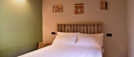 Una cama bien tendida con sábanas blancas en una habitación con cabecera de madera y pared verde.