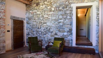 Una habitación con pared de piedra, dos sillas de madera, un banco de madera y una puerta de madera.