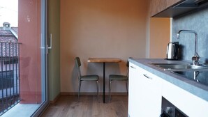 Pieni keittiö, jossa on puinen pöytä ja kaksi tuolia, pesuallas ja ikkuna, josta on näkymä parvekkeelle.