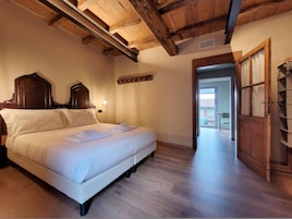 Un dormitorio con techo de madera, una cama con ropa de cama blanca, un armario de madera y vistas al exterior.
