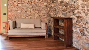Un sofá de madera con un cojín, una pared de piedra, una mesita de madera y una estantería de madera.