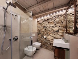 Un baño moderno con ducha de vidrio, un bidé y una pared de piedra.