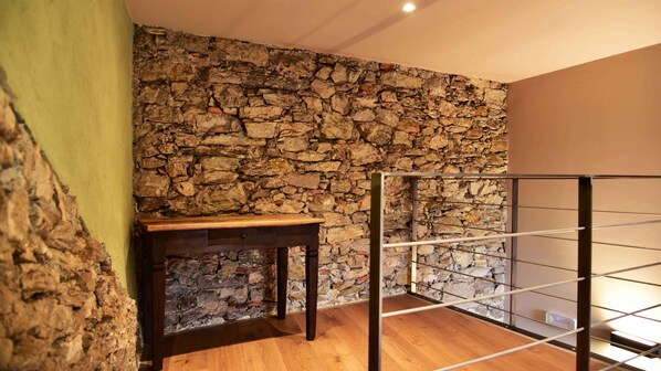 Um quarto com parede de pedra, uma mesa de madeira e uma estante de metal.