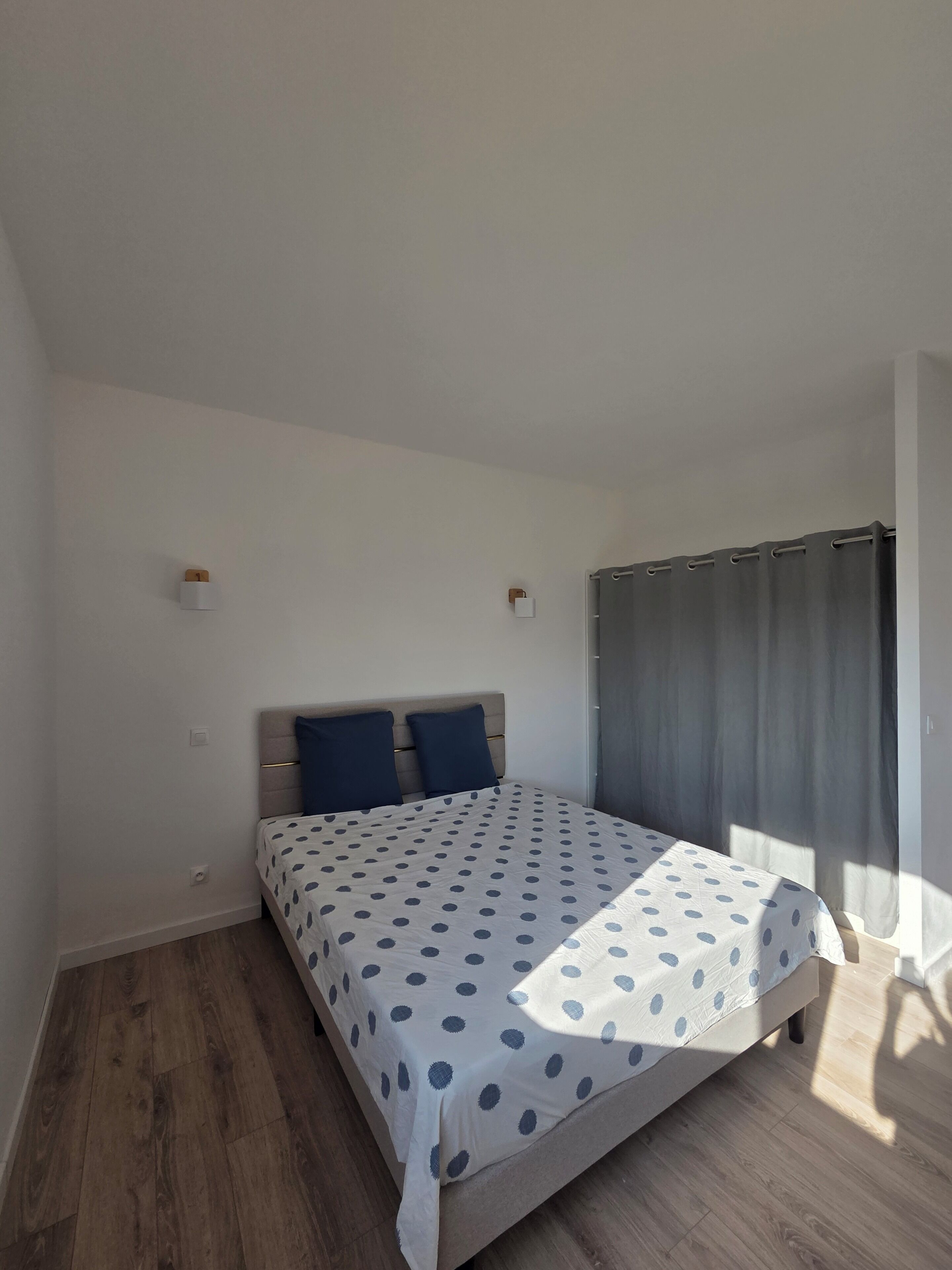 Une chambre à coucher avec un lit, une tête de lit, une fenêtre avec des rideaux et un plancher en bois.