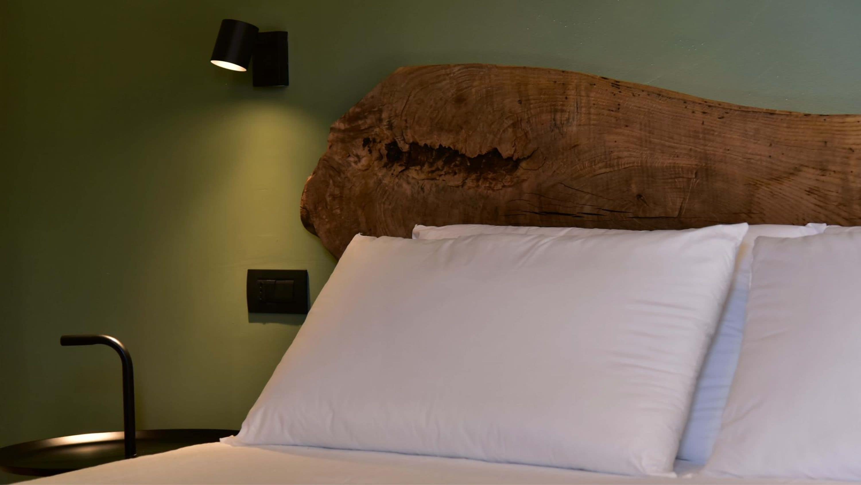 Ein Bett mit weißen Leinen, einem Holz-Kopfteil, einer Wandlampe und einem Bedienfeld an der Wand.