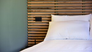 A bed with white linens and a wooden headboard with horizontal slats. - Ronchetto - Appartamento Atticus (Cunardo)