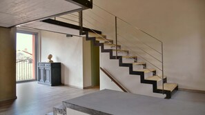Una escalera moderna con barandillas de vidrio y peldaños de madera, que conduce a un balcón con vistas al exterior.