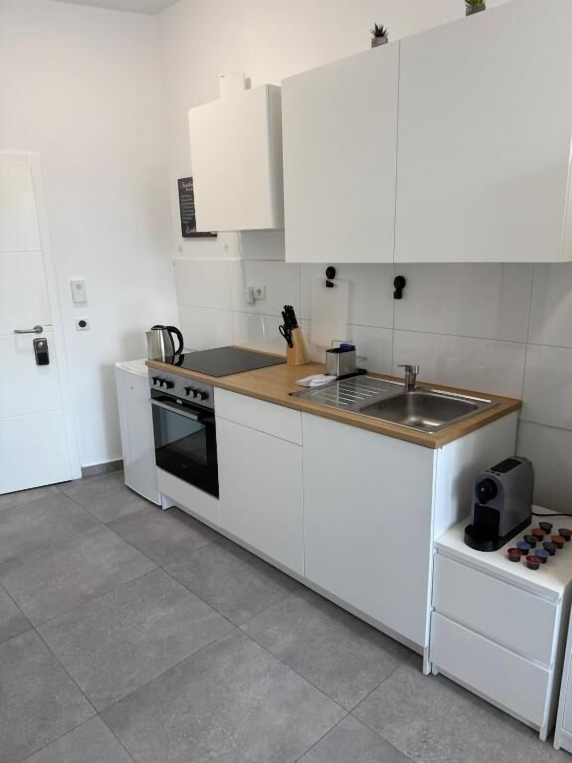 Une cuisine compacte avec des meubles blancs, un plan de travail en bois, un four encastré, un évier et un grille-pain.