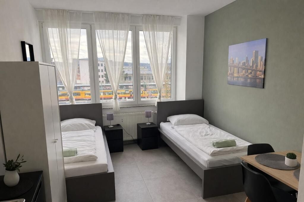 Habitación de hotel con dos camas, un escritorio, una silla, un radiador y una ventana con vista a la ciudad.