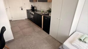 A compact room with a kitchenette, a bed, and a chair.
