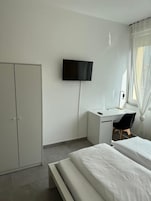 A bedroom with a bed, a desk, a chair, a TV, and a wardrobe.