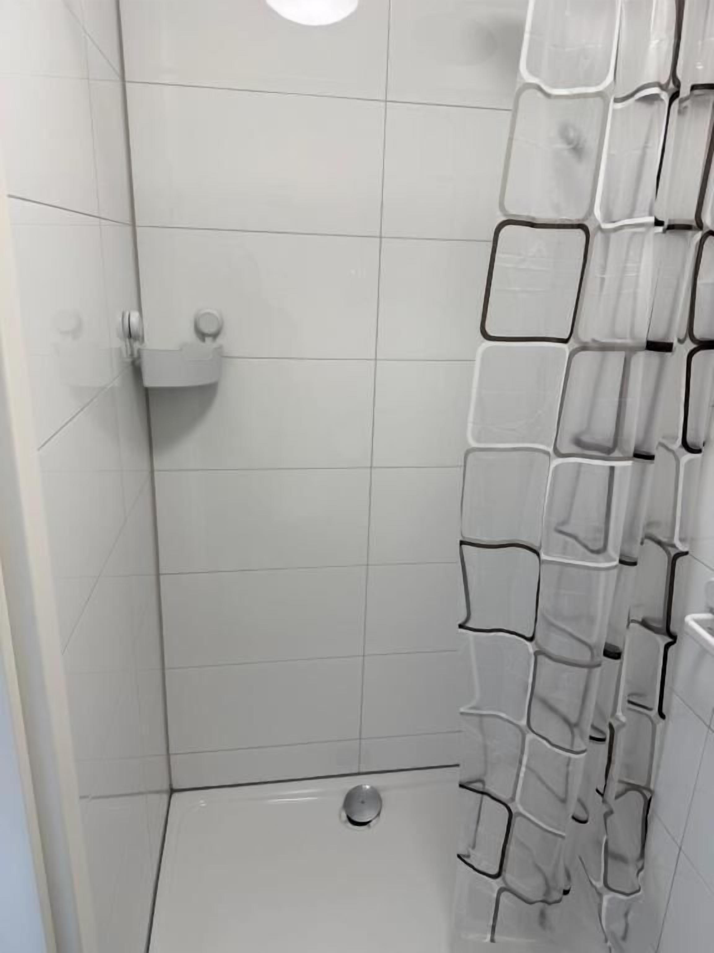 Un espace douche avec des murs recouverts de carreaux blancs et un rideau de douche à motifs géométriques.