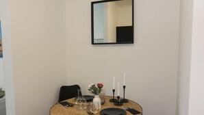 A dining area with a round table set for two, a mirror above, and a vase with flowers on the table.