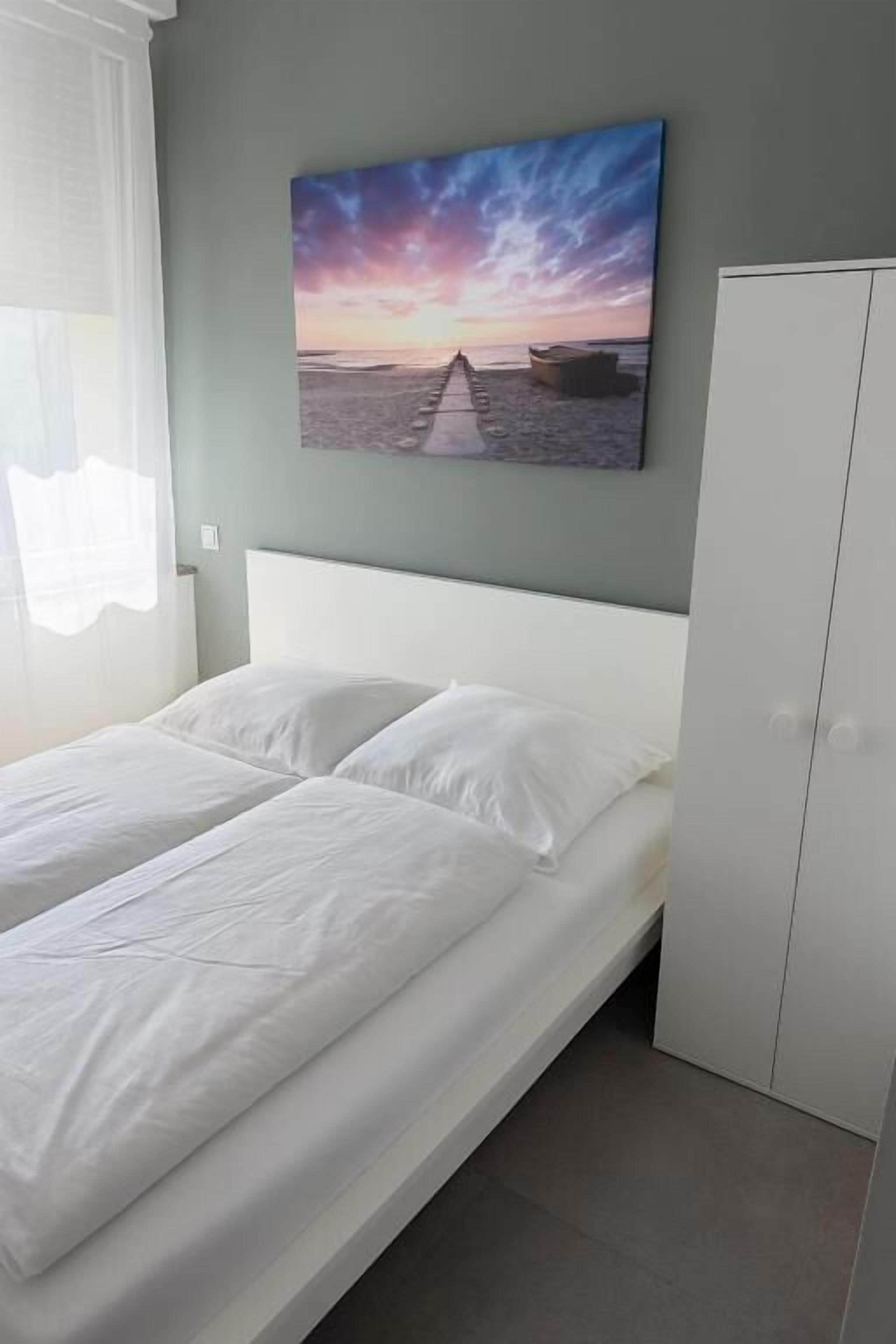 Une chambre à coucher comprenant un lit, une armoire et un tableau représentant une scène de plage, accroché au mur.