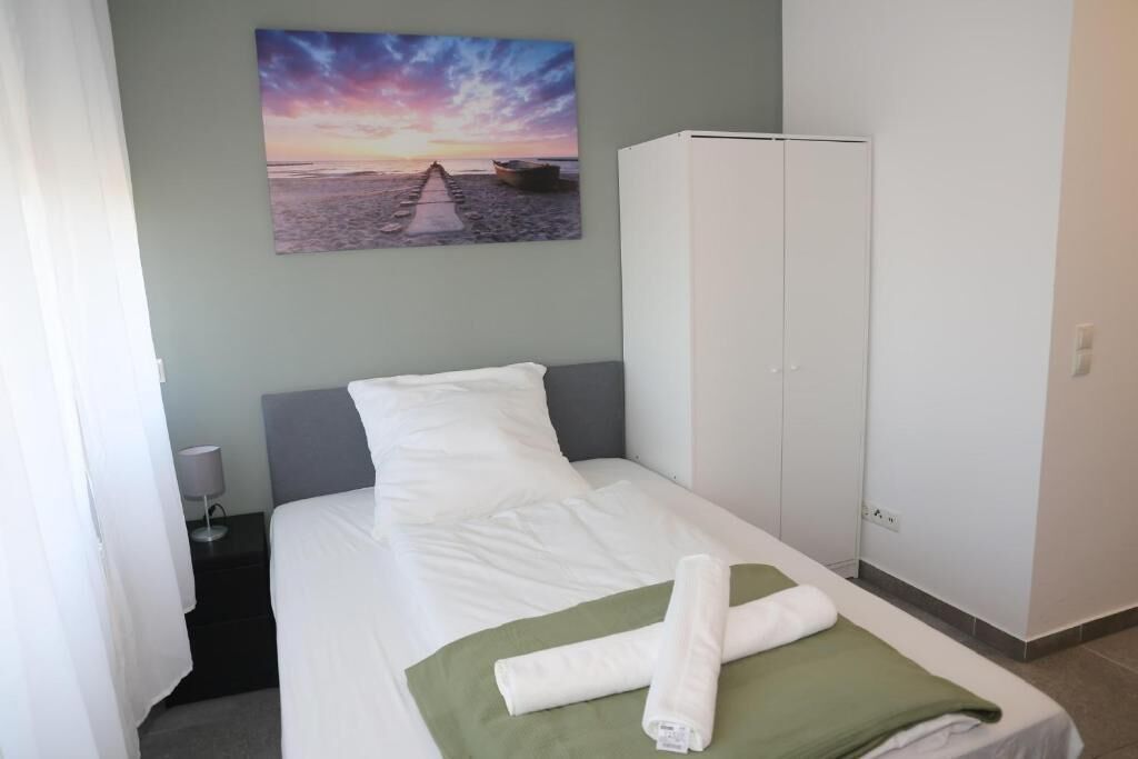 A hotel room with a bed, a wardrobe, a nightstand, and a painting of a sunset over the sea.