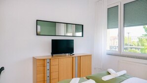 A hotel room with a bed, a TV on a wooden cabinet, a window with blinds, and a radiator.