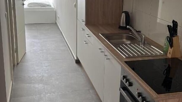 A narrow kitchen with a stove, sink, and wooden cabinets.