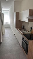 A narrow kitchen with a stove, sink, and wooden cabinets.