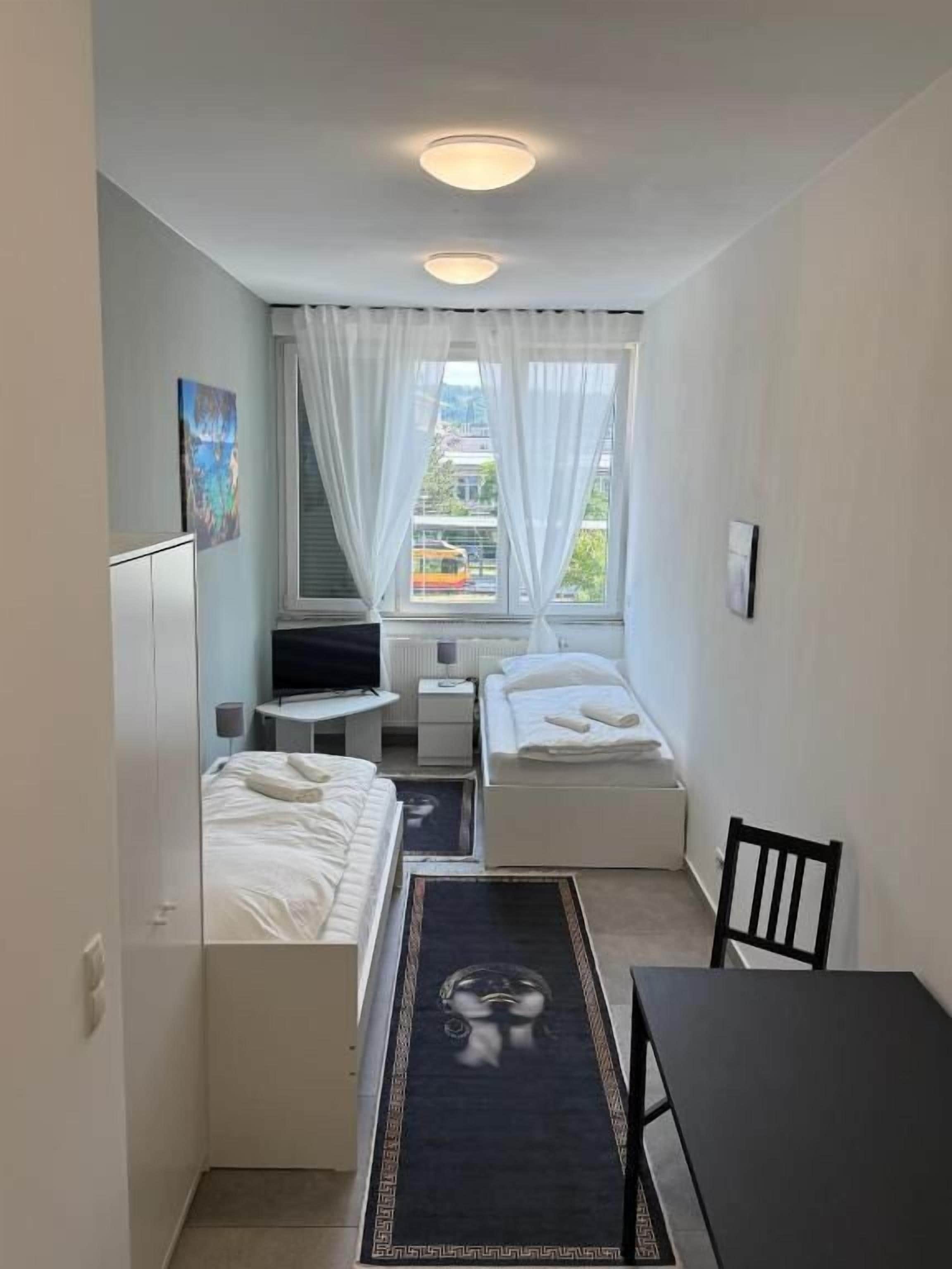 Une chambre d’hôtel de taille réduite, comprenant un lit, un bureau, une chaise, une télévision et une fenêtre avec des rideaux.