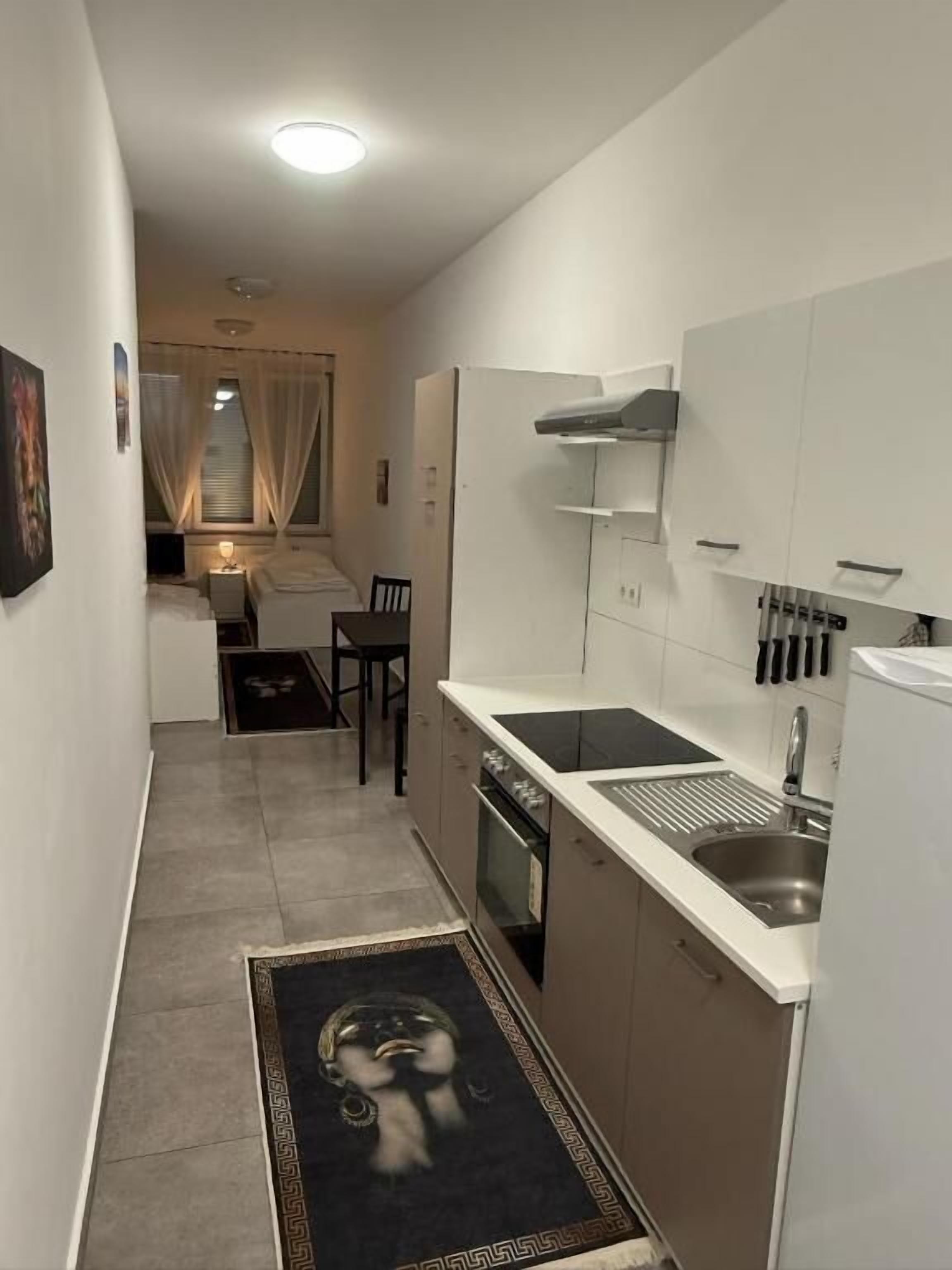A narrow kitchen with a sink, cabinets, and a window with curtains.