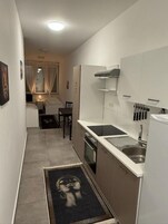 Cocina estrecha con un lavamanos, armarios y una ventana con cortinas.