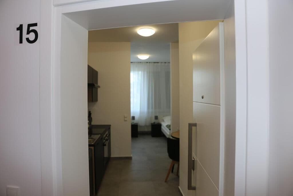 Un couloir avec le numéro 15 peint sur le mur, qui mène à une pièce contenant un lit et une fenêtre avec des rideaux.