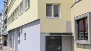 A multi-story building with a flat facade, a ground-level entrance, and a window on the right side.